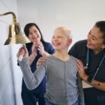 A young child girl chemotherapy patient in a treatment office, celebrating the completion of her treatment with a ceremonial bell ring. Actor portrayal.
