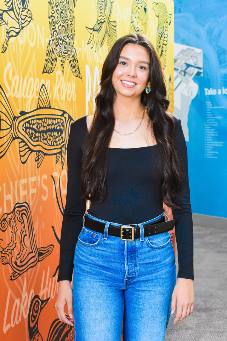 Photograph of Ireland Smith standing by the mural at the Bruce Power Visitors' Centre.