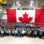People stand in front of feeders and large Canadian Flag at BWXT in Cambridge.