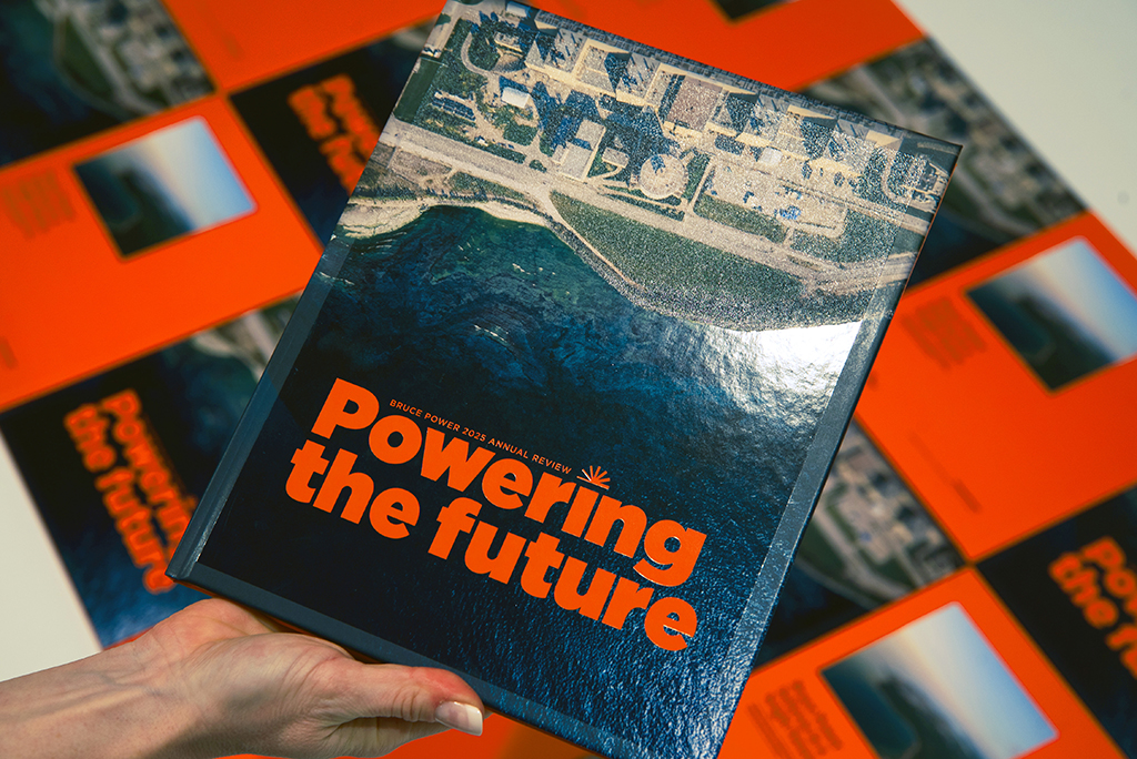 Hand holding Bruce Power's Annual Report Powering the Future with pages displayed in background.